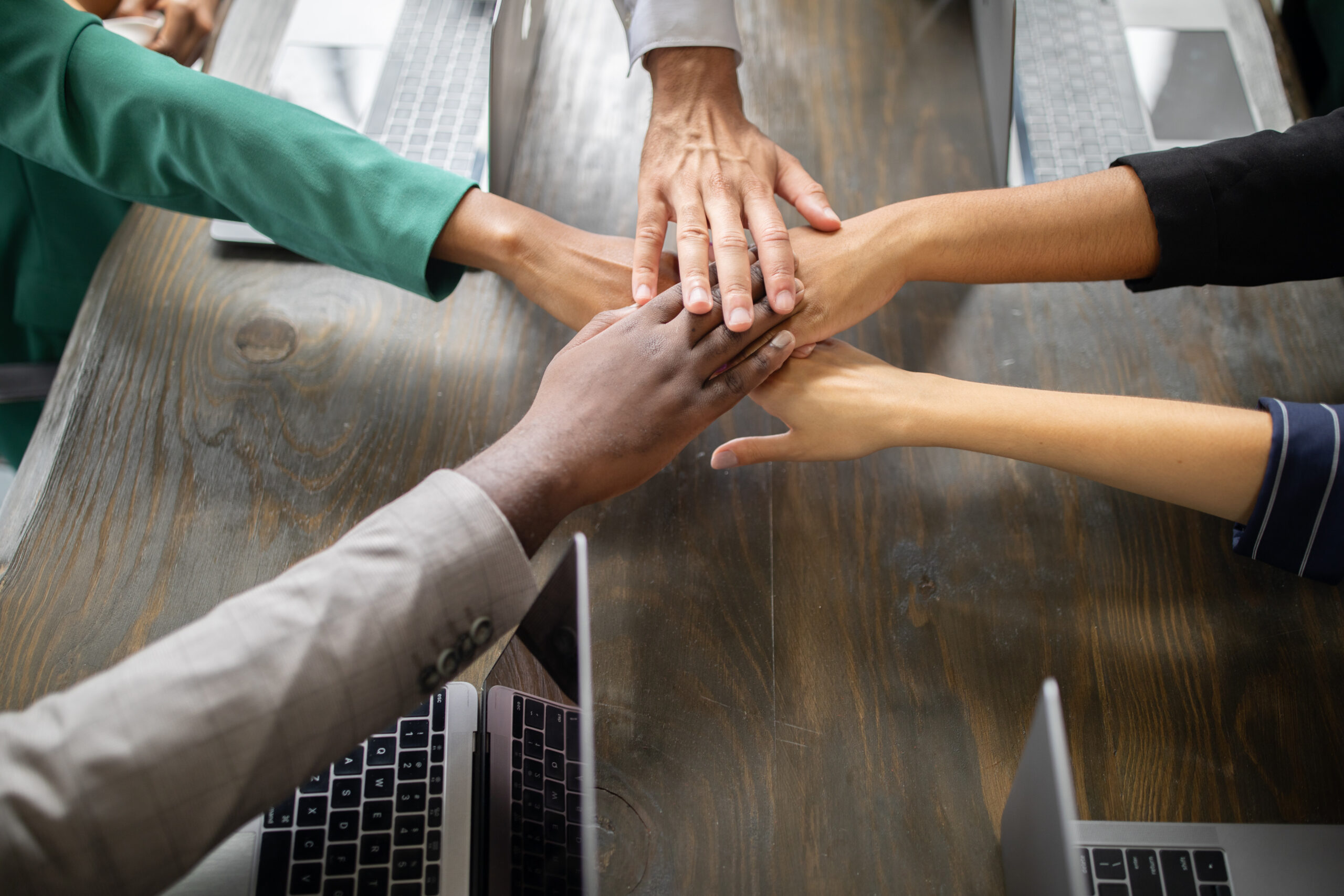 Diverse team members gather around a table in a corporate office, joining hands in a show of cooperation and commitment to success during a productive business meeting.